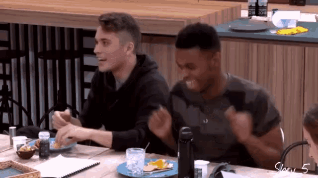 two men are sitting at a table with a plate of food and a bottle of water