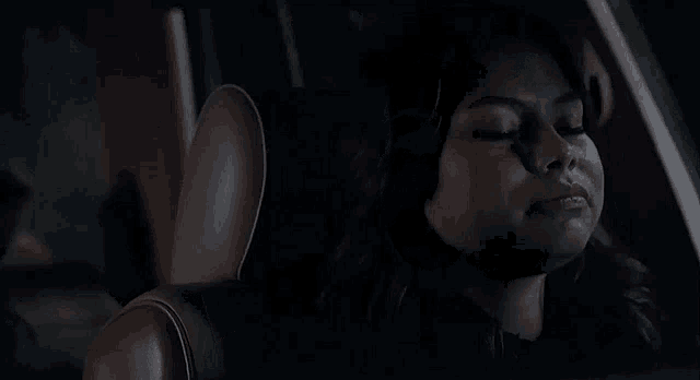 a woman is sitting in the back seat of a car at night with her eyes closed .
