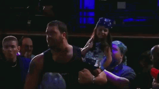 a man in a black tank top is holding a little girl in his arms in a boxing ring .