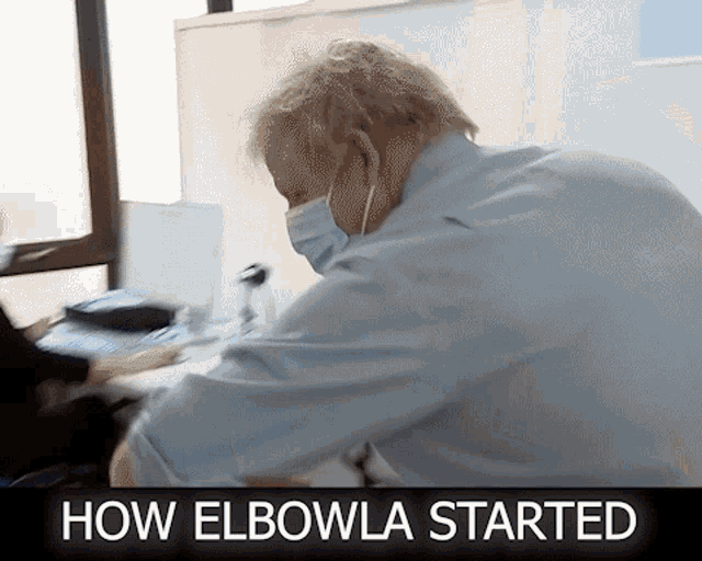 a man wearing a mask is sitting at a desk with the words how elbowla started below him