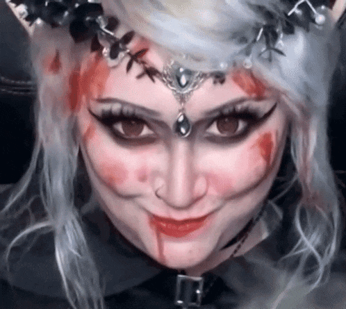 a woman with blood on her face and a crown on her head is smiling .
