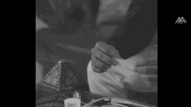 a black and white photo of a person rolling a cigarette on a table .