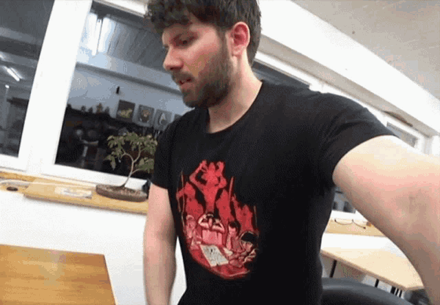 a man with a beard wears a black t-shirt with a picture of a group of people sitting around a table