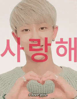 a young man is making a heart shape with his hands and the words i love you are behind him