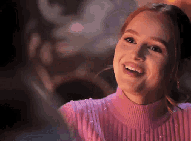 a woman wearing a pink sweater is smiling and looking at the camera .