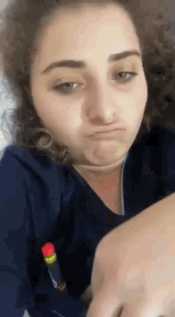 a woman with curly hair is making a funny face while holding a pen in her pocket .