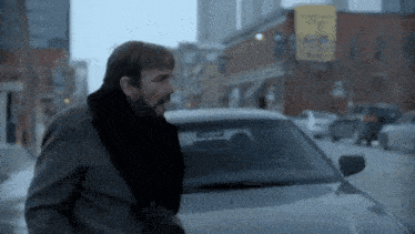 a man with a scarf around his neck is standing next to a car on a city street