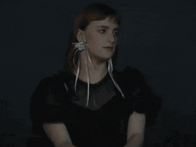 a woman wearing a black dress and white earrings looks to the side