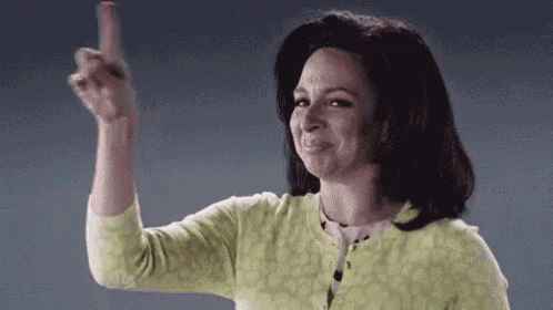 a woman in a green sweater is pointing her finger up .