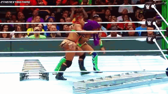 two female wrestlers are fighting in a wrestling ring with a crowd watching .