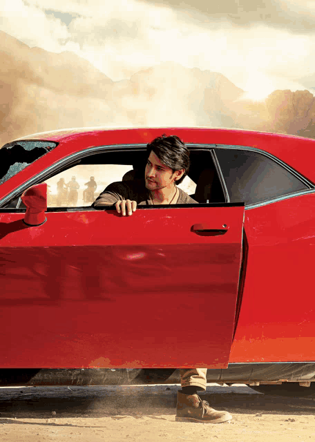 a man leaning out of a red car with mountains in the background