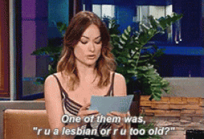 a woman is sitting at a table holding a piece of paper and saying one of them was ru a lesbian or ru too old