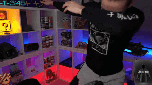 a man in a black shirt with a skull on it is dancing in front of a shelf that says 3:46