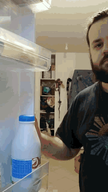 a man in a black shirt is reaching into a fridge to take a bottle of milk