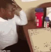 a man is sitting at a desk holding his head .
