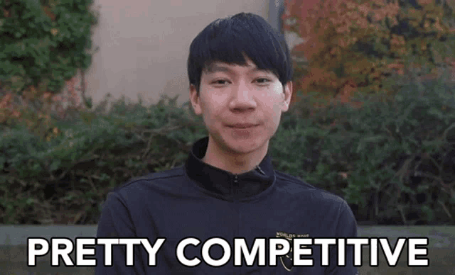 a man in a black jacket says pretty competitive in front of a bush