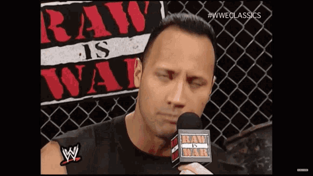 a man talking into a microphone with a raw is war sign behind him