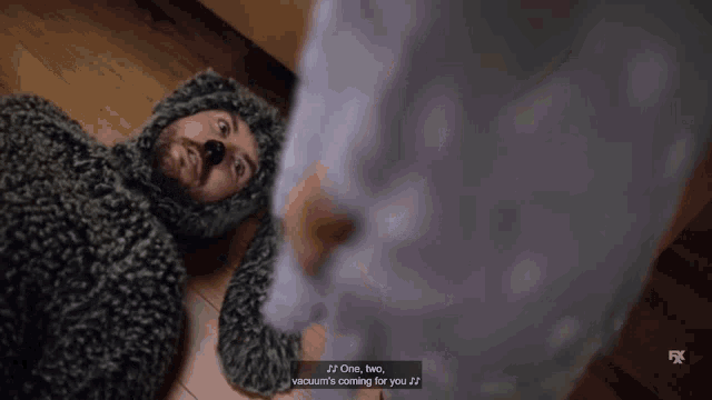 a man in a furry animal costume is laying on the floor and says " one two vacuum 's coming for you "