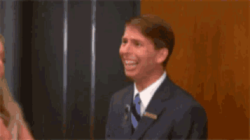 a man in a suit and tie is laughing while a woman looks on .