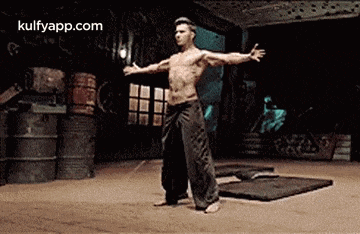 a man without a shirt is standing on a mat with his arms outstretched in a gym .