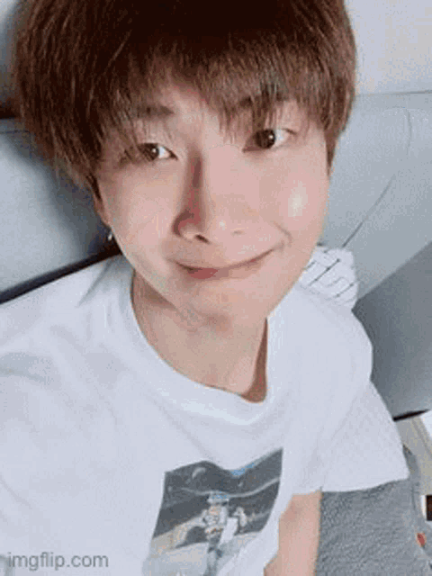 a young man wearing a white t-shirt is sitting on a bed and smiling .