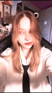 a girl with long red hair is taking a selfie while wearing a tie .