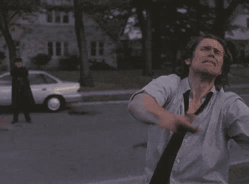 a man in a white shirt and tie is standing in front of a car that is exploding .