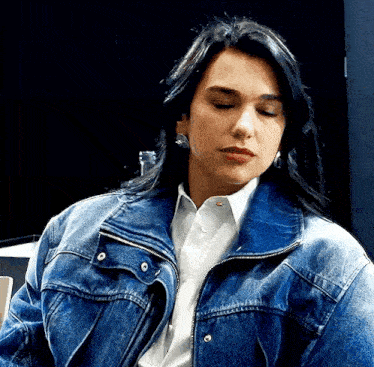 a woman wearing a blue denim jacket and a white shirt is sitting down .