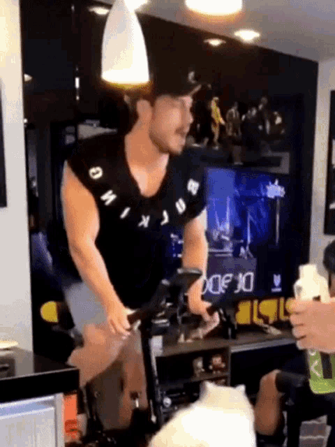 a man is riding an exercise bike in a living room while wearing a shirt that says omix