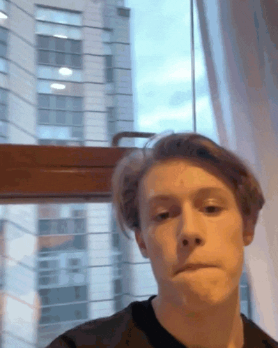 a young man standing in front of a window making a face