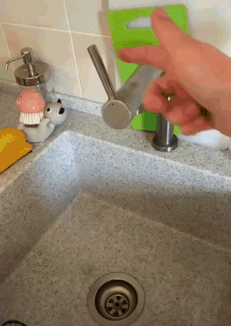 a person is pressing a button on a faucet in a kitchen sink