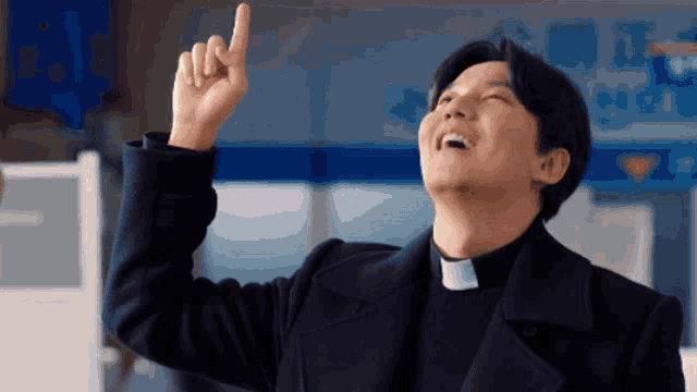 a man wearing a priest collar points upwards with his finger