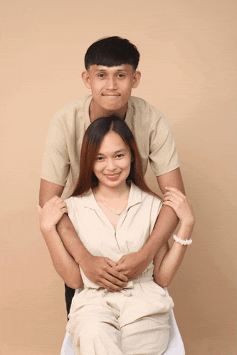 a man and woman posing for a picture with the woman sitting on a chair