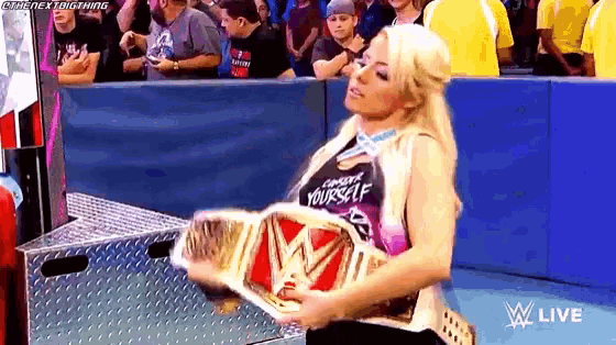 a woman is holding a wrestling championship belt while standing in a ring .