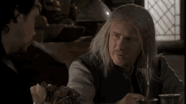 a man with gray hair is sitting at a table with another man and the word de is on the screen