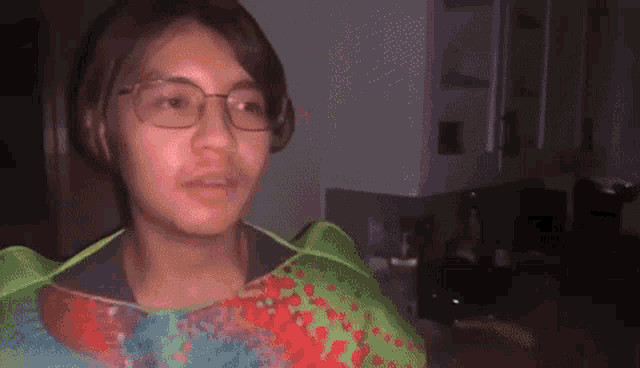 a young man wearing glasses and a green apron is standing in a dark room in a dark room .