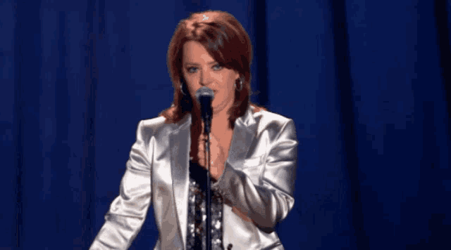 a woman singing into a microphone while wearing a white jacket