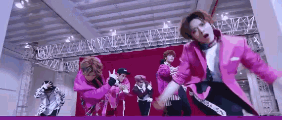 a group of young men are dancing on a stage in a pink jacket .