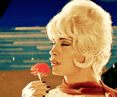 a woman with blonde hair is holding a small red flower in her hand