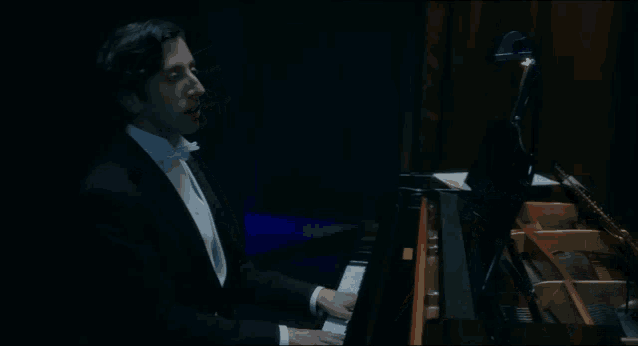 a man in a tuxedo is playing a piano in the dark