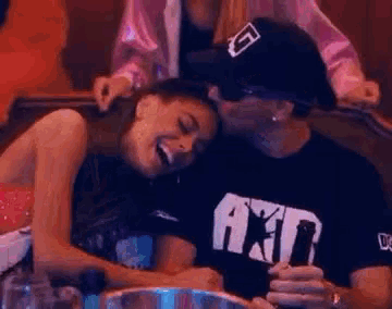 a man is kissing a woman on the cheek while sitting at a table in a bar .