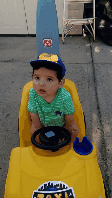 a baby is sitting in a yellow toy car that says taxi on it