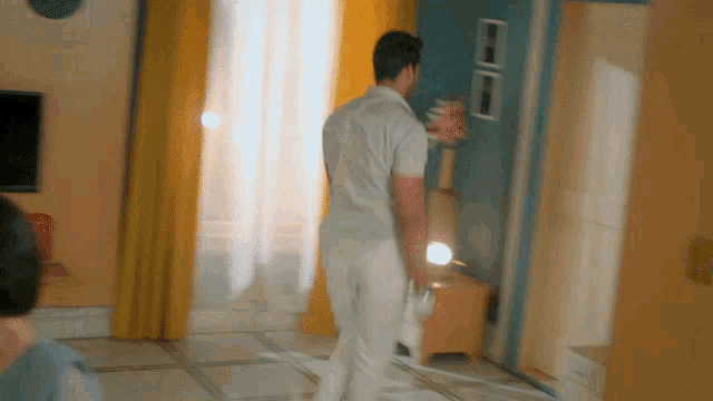 a man in a white shirt and white pants is walking through a living room