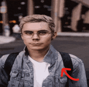 a young man wearing glasses and a denim jacket has a red arrow pointing to his left