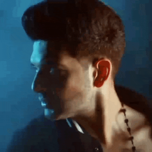 a man with a necklace around his neck is looking at the camera in a dark room .