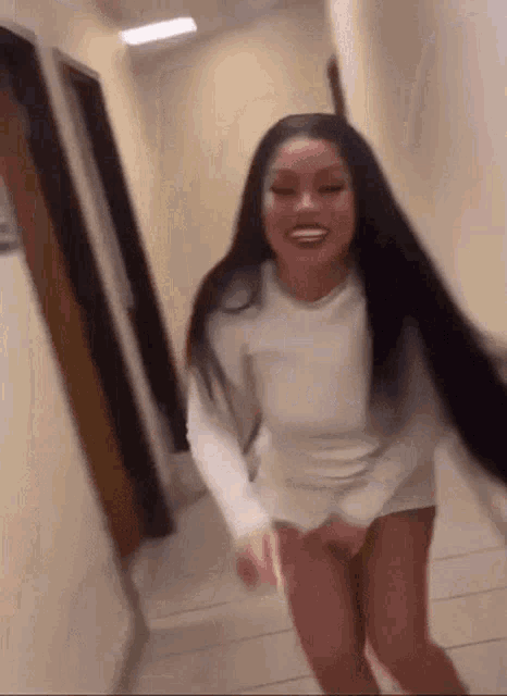 a woman with long black hair is standing in a hallway wearing a white dress and shorts .