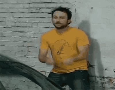 a man in a yellow shirt is leaning against a brick wall .