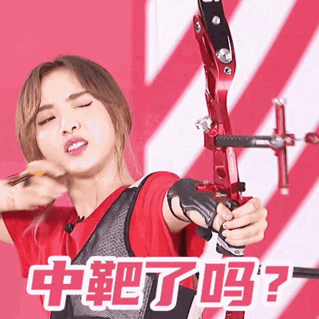 a woman in a red shirt is holding a red bow and arrow with chinese writing behind her