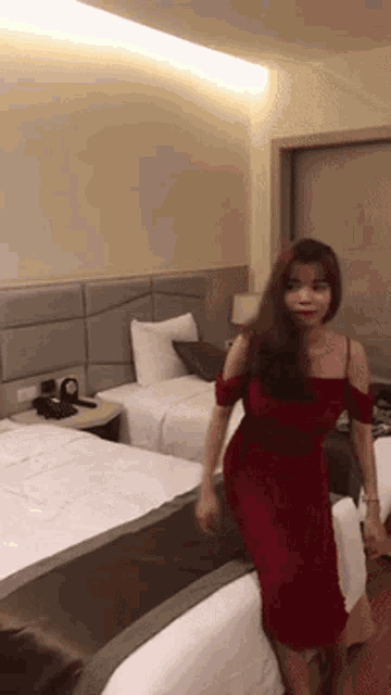 a woman in a red dress is standing next to a bed