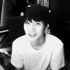 a young man wearing a hat and a white shirt smiles in a black and white photo